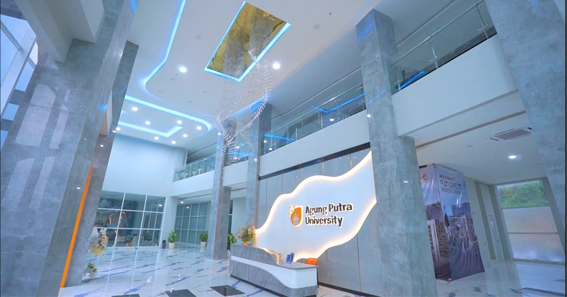 Lobi kampus APU dengan meja resepsionis dan tulisan Agung Putra University di dinding